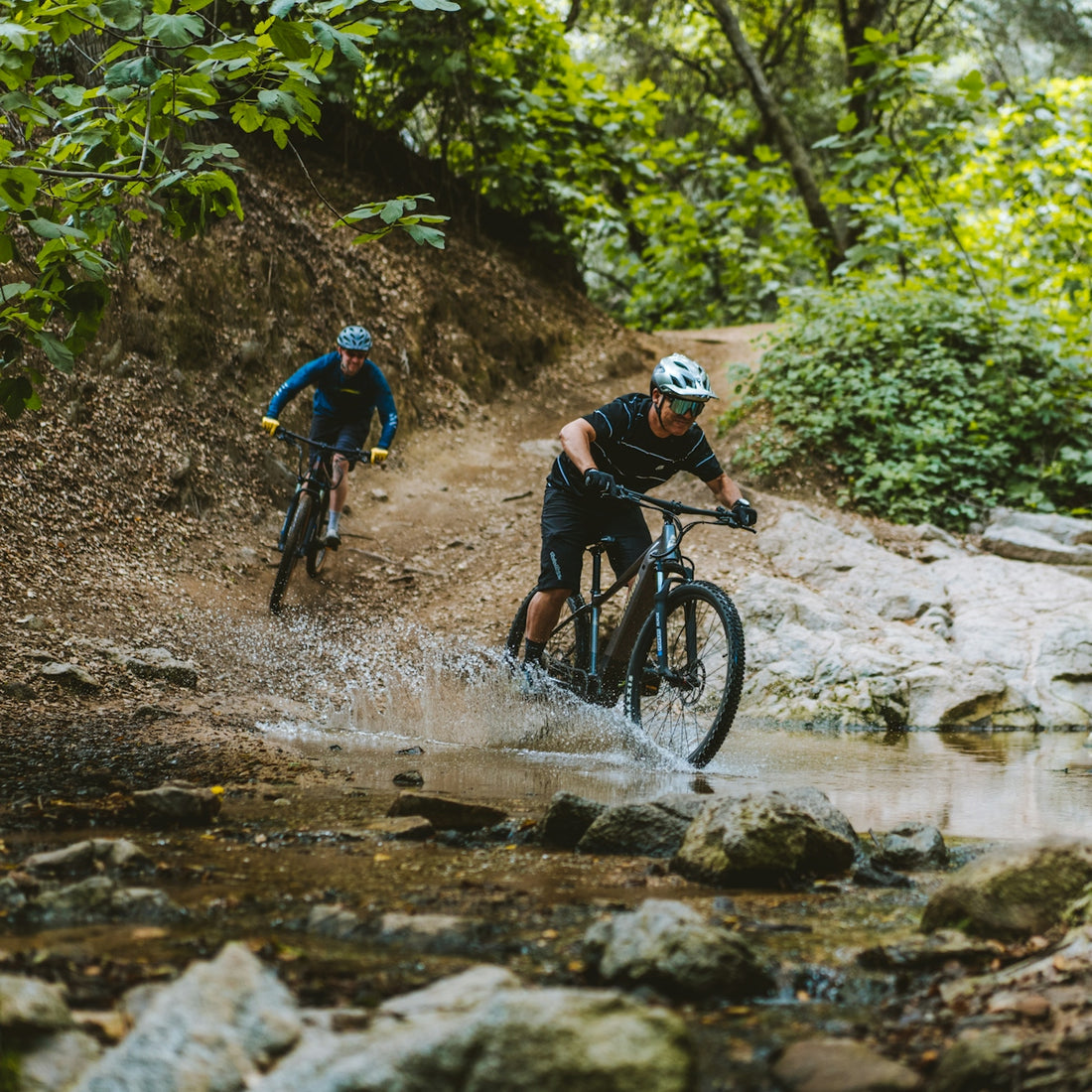 a couple of people riding bikes through a creek
