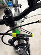Close-up of bicycle handlebars and front frame with attached cables secured by two Brake and Shift Cable Clips (pack of 5). A headlight is mounted on the front fork, with a blurred indoor background.