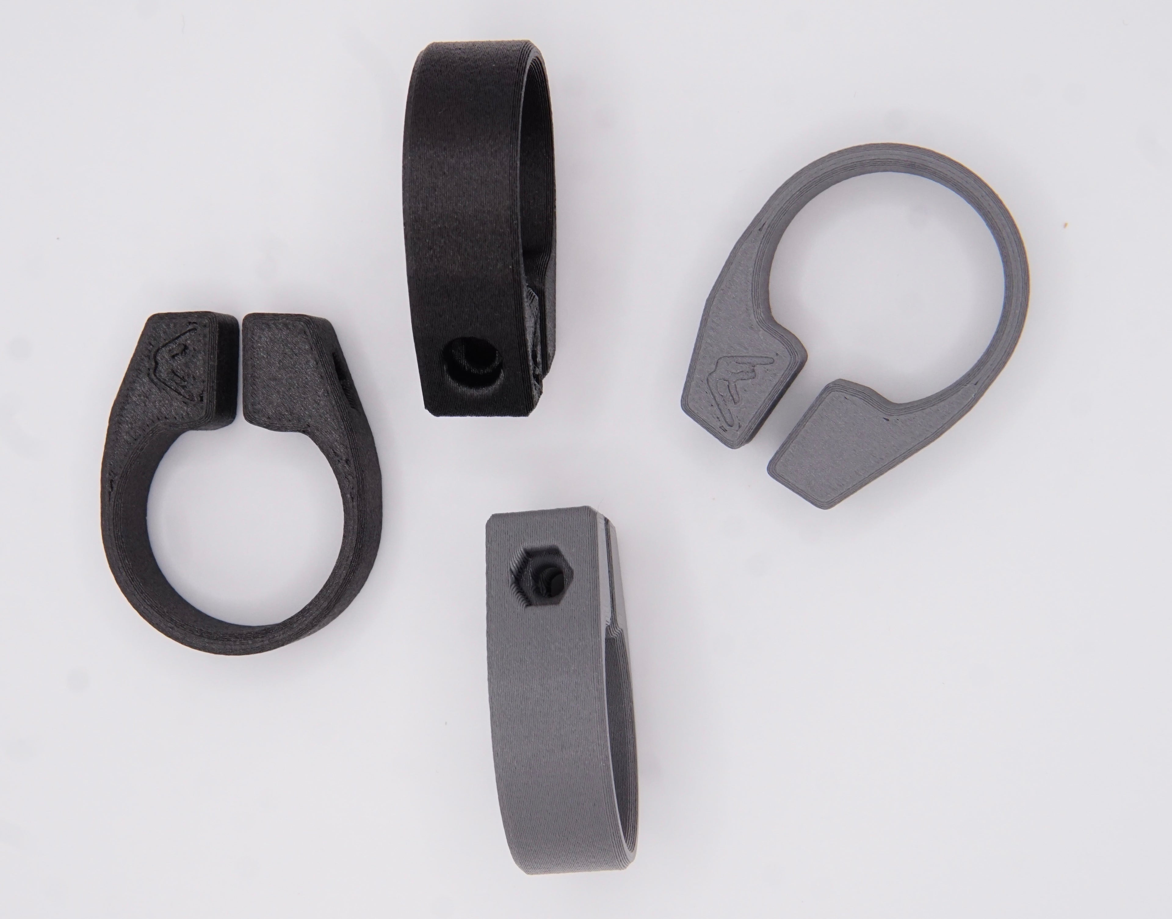 Four clamp-style rings—two black, two gray—are shown on a white background. These interchangeable spare clamps for MTB AirGrips bar clamps each have a small emblem and tightening hole.