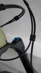 Close-up of black bicycle cables secured with a Brake and Shift Cable Clip (pack of 5), with part of the bike frame and a blue bolt visible in the background.