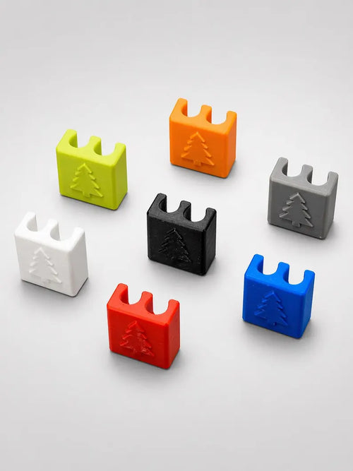 A set of five Brake and Shift Cable Clips, shaped like small blocks with a tree symbol on each. The clips come in green, orange, gray, white, and black, shown arranged on a light gray surface.